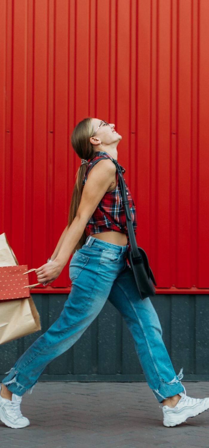 Happy girl with shopping paper bag on red wall shop background. Young woman holding shopping bag full of groceries and purchases after shopping.