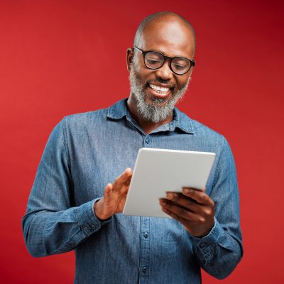 One happy mature african american man isolated against a red background in a studio and browsing th.